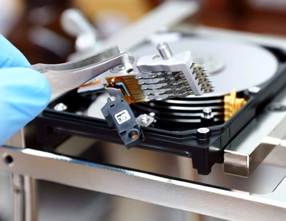 Close-up of a technician removing the read/write head assembly from an open hard drive